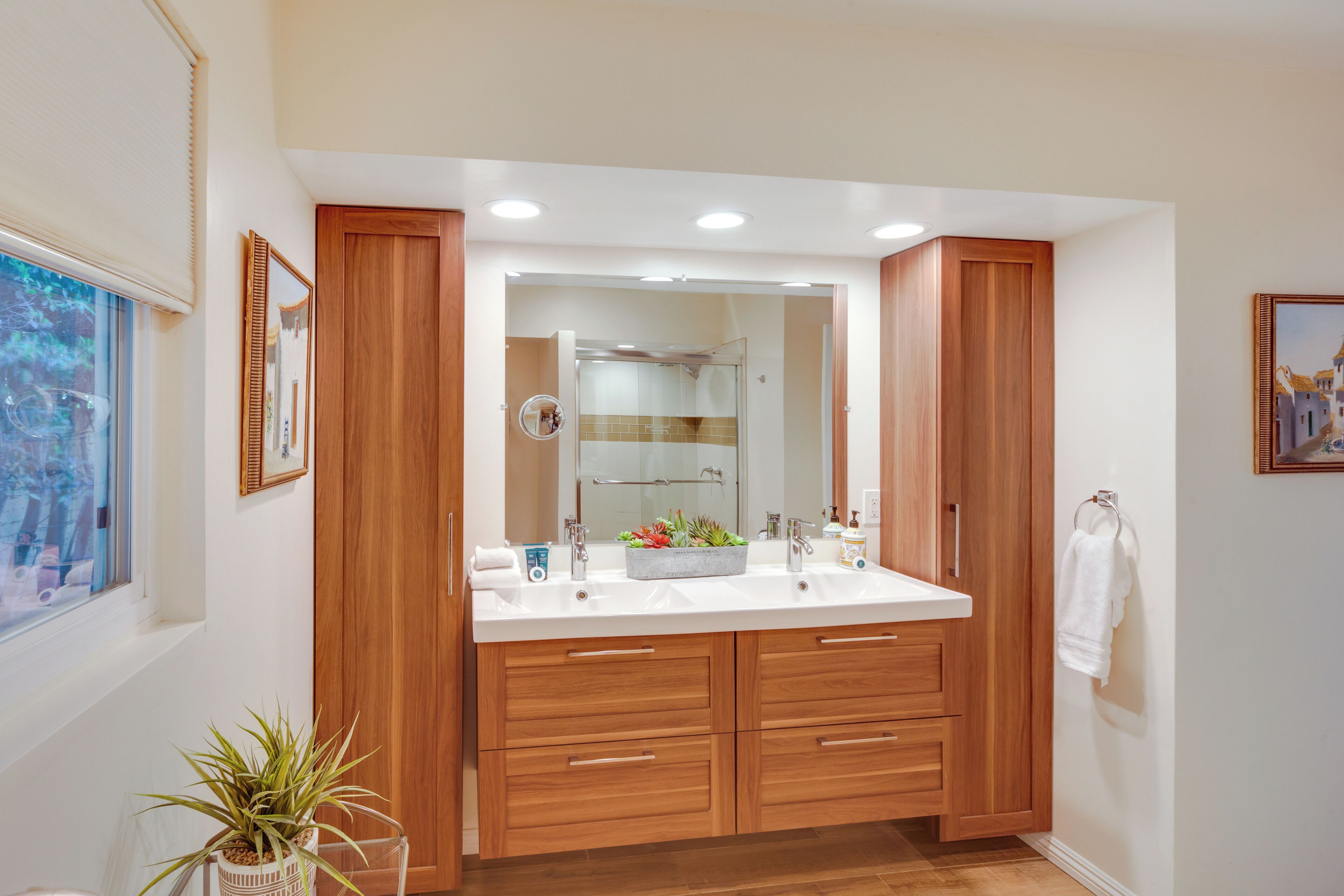 A modern bathroom with wooden cabinetry, a large mirror, and a white countertop.