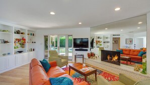 A spacious living room with a leather sofa, a flat-screen TV, a fireplace, and a large mirror reflecting the room. - Patio, Pool & Mountain Views: Palm Springs Home! (Palm Springs)