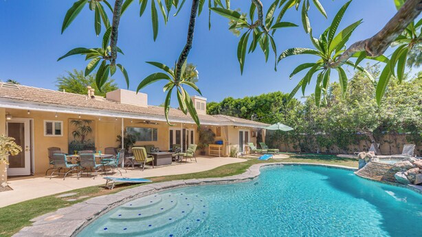 A swimming pool with a curved edge, surrounded by a patio with chairs and a table. - Patio, Pool & Mountain Views: Palm Springs Home! (Palm Springs)