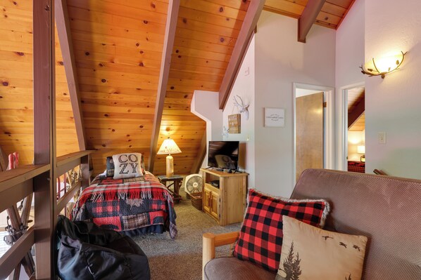 A cozy cabin interior with a loft bed, a wooden dining table, a sofa, and a television.