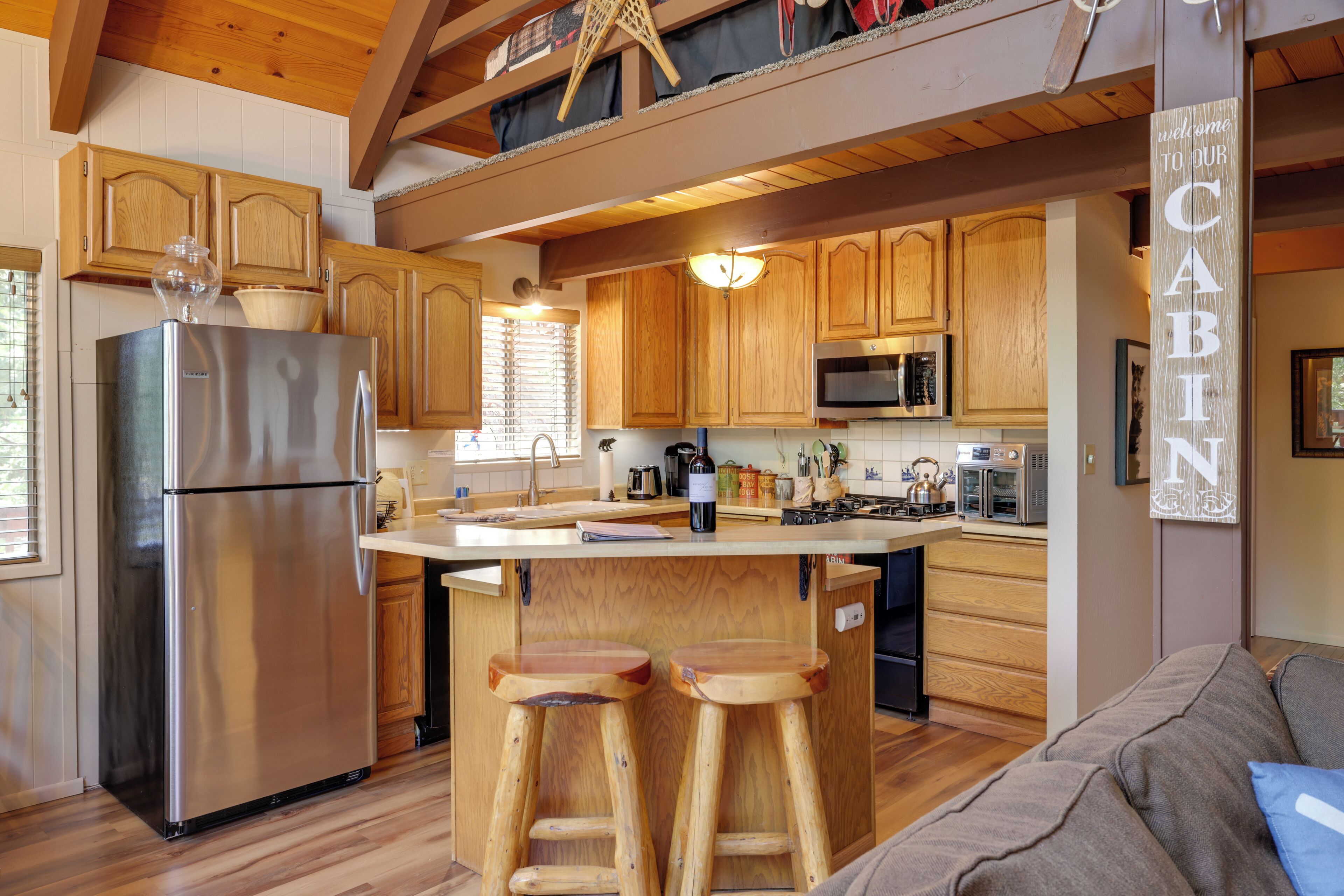 A kitchen with wooden cabinets, a stainless steel refrigerator, wooden stools, and a central island.
