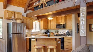 Une cuisine avec des meubles de rangement en bois, un réfrigérateur en acier inoxydable, des tabourets en bois et un îlot central.