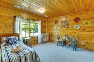 Una habitación acogedora con cama, escritorio y sillas, paredes de madera y una ventana con cortinas.