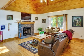 Ein Wohnzimmer mit Kamin aus Stein, einer Ledersofa, Holzböden und einem an der Wand befestigten Fernseher.