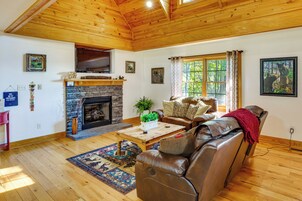 Una sala de estar con chimenea de piedra, sofá de cuero, piso de madera y un televisor montado en la pared.