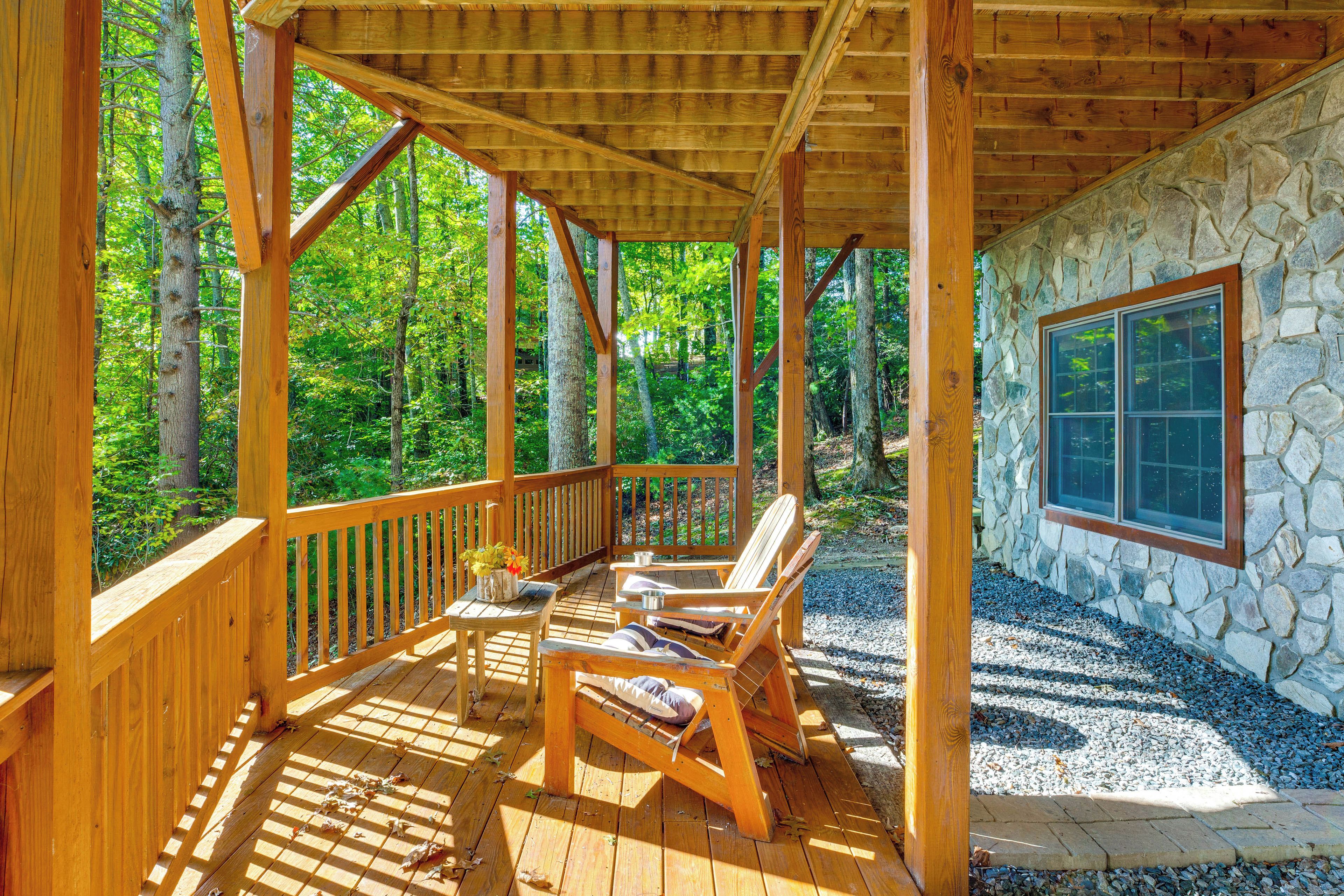 Une terrasse en bois avec un mur en pierre et une fenêtre, le tout entouré d’arbres.