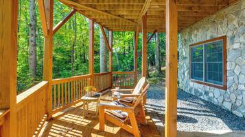 Une terrasse en bois avec un mur en pierre et une fenêtre, le tout entouré d’arbres.