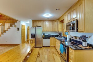 Eine Küche mit Holzausstattung, Edelstahlgeräten, einem Holzessttisch und einer Treppe.