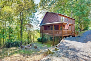 Une cabane dotée d’une terrasse, entourée d’arbres et bordée d’un chemin de gravier.