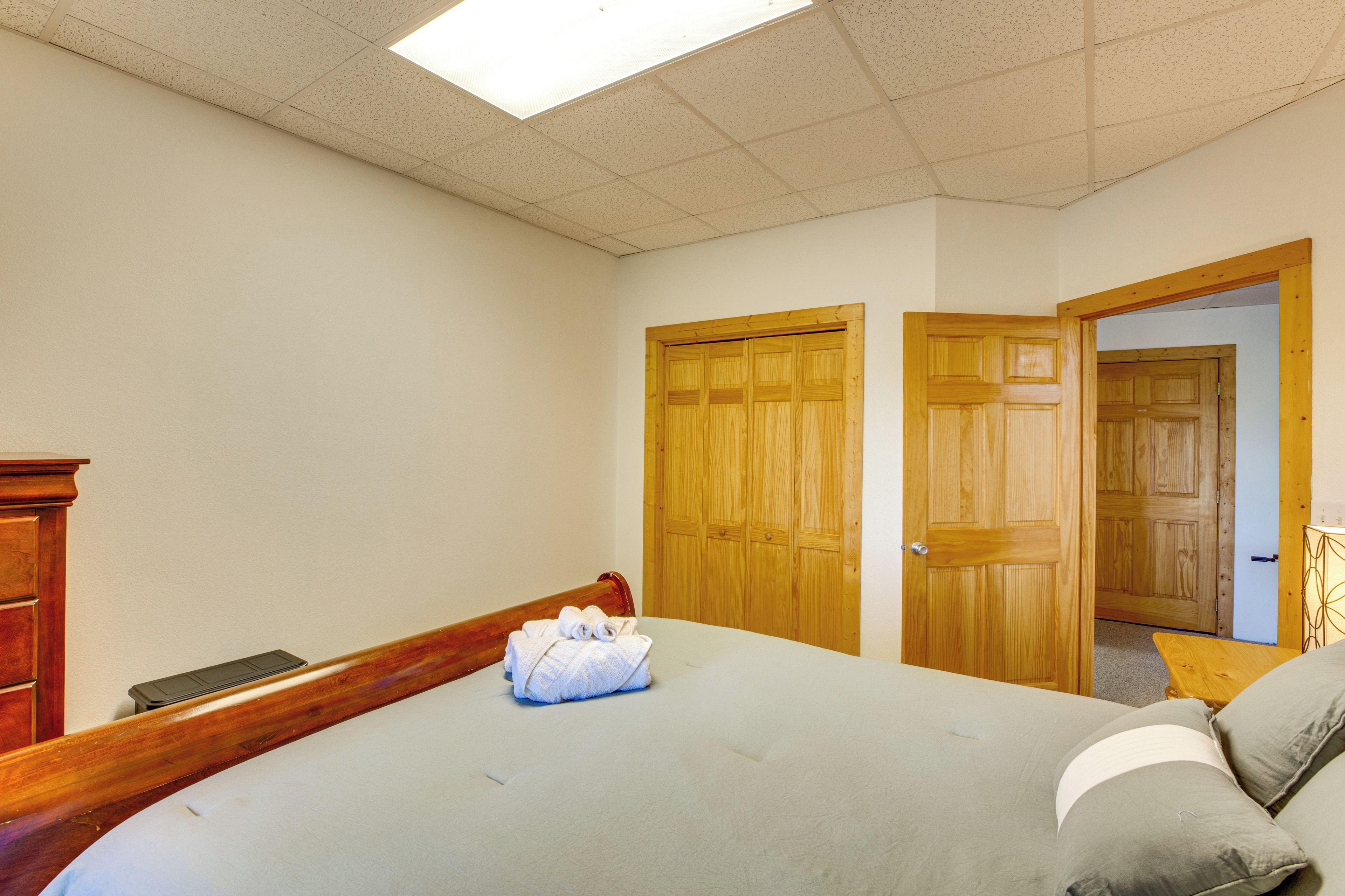 A bedroom with a bed, a wooden wardrobe, and a door leading to another room.