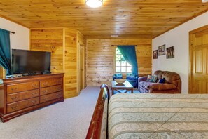A log cabin interior with a wooden ceiling, a television on a dresser, a sofa, a bed, and a window with curtains. - 'A Bit of Heaven' Cabin < 13 Miles From Boone! (Fleetwood)