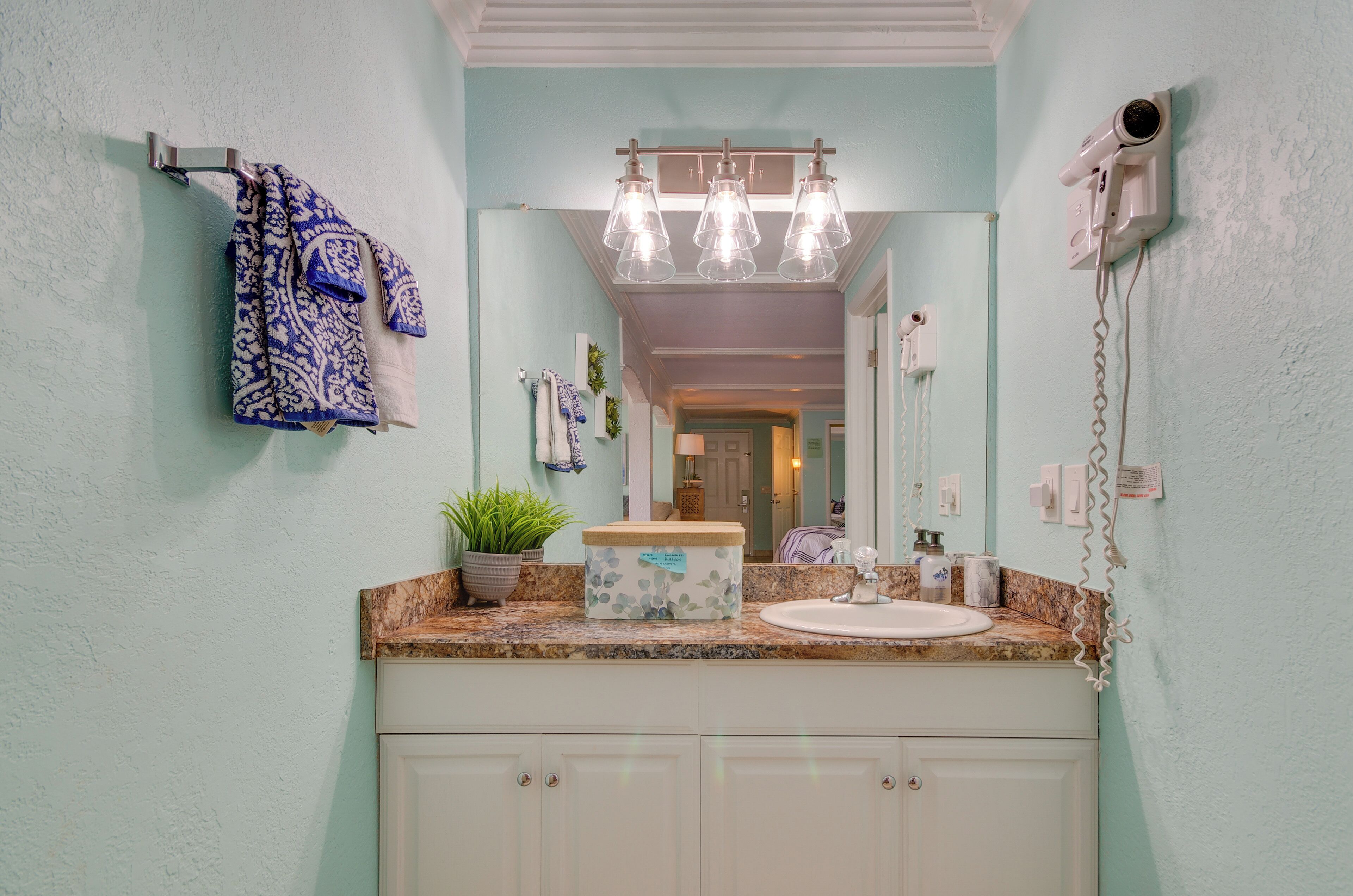 A bathroom with a sink, mirror, towel rack, and a hairdryer mounted on the wall.