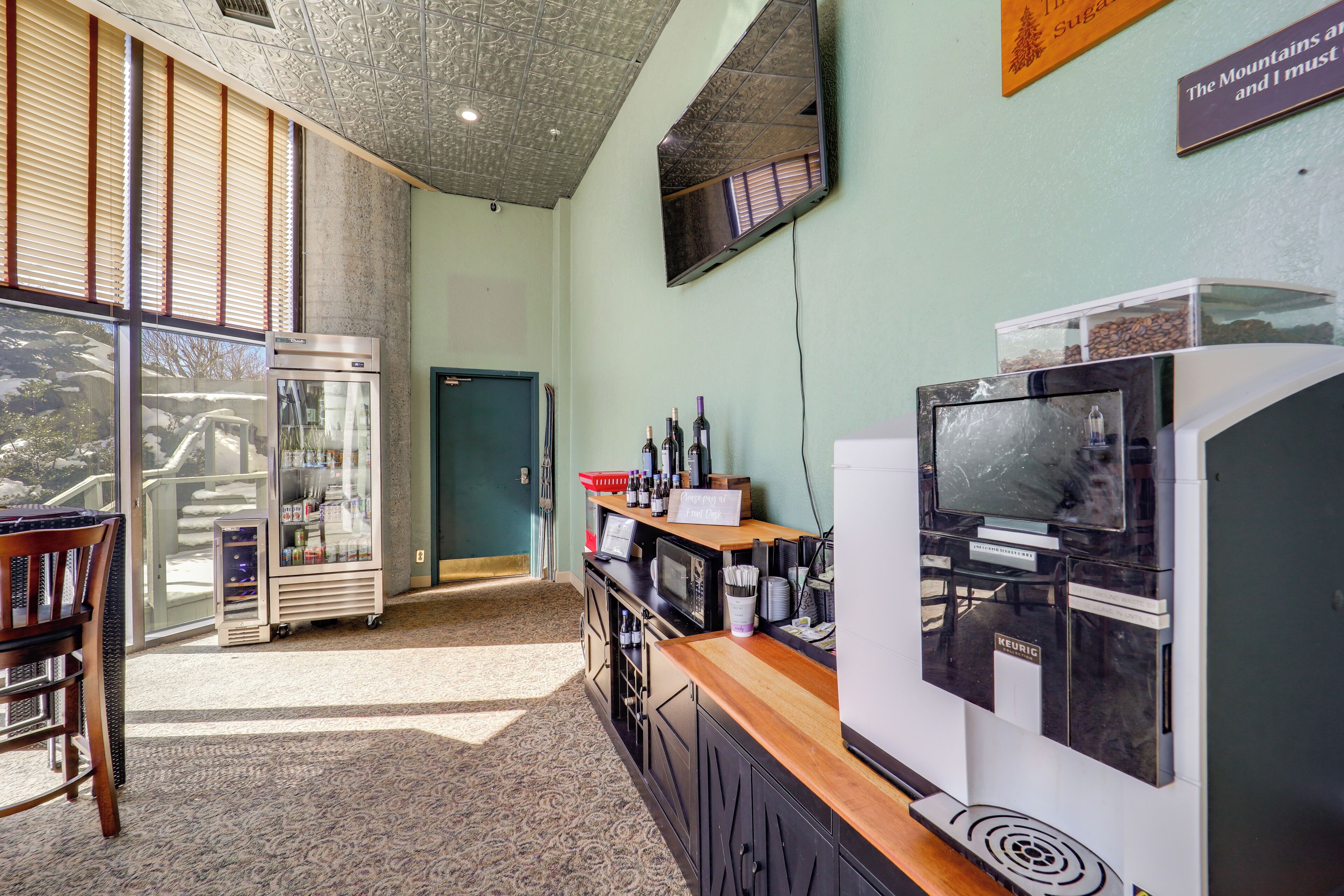 Une chambre d’hôtel équipée d’une kitchenette, d’une télévision et d’une grande fenêtre avec des stores.