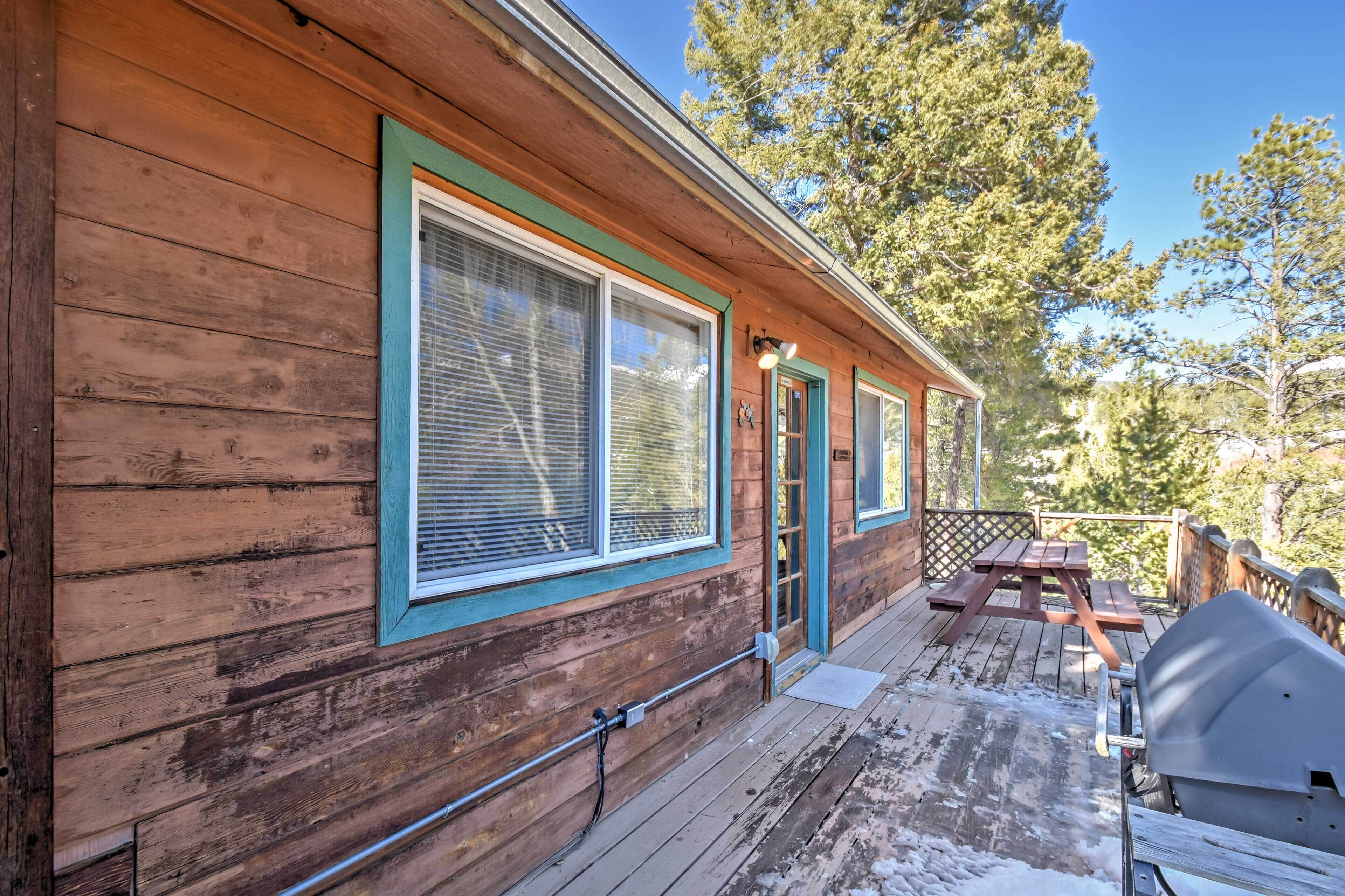 A wooden cabin with large windows, a deck with a grill, and a picnic table.