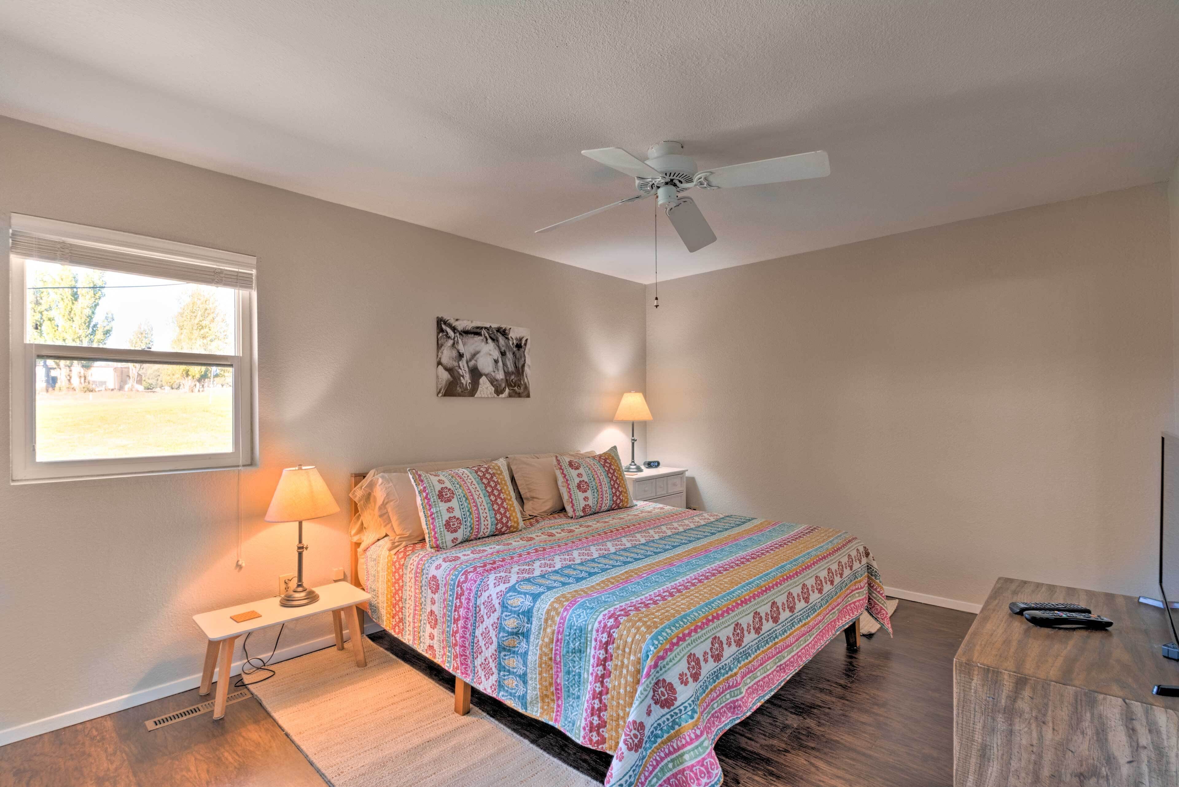 A bedroom with a bed, bedside table, lamp, ceiling fan, and a TV stand.