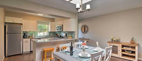 Una cocina moderna con una isla central, suelo de madera y una zona de comedor con mobiliario blanco.