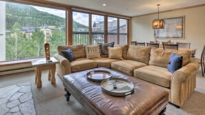 A cozy living room with a large sectional sofa, a glass coffee table, and a view of a mountainous landscape through large windows. - Spacious Vail Condo: Steps From Eagle Bahn Gondola (Vail)