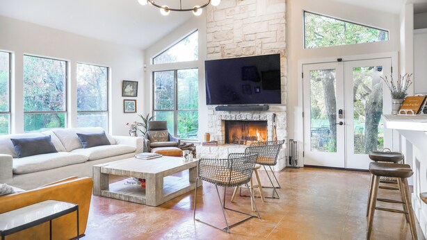 A spacious living room with a stone fireplace, large windows, and a television mounted above it. - Shaded Getaway w/ BBQ & Fire Pit in Austin! (Austin)