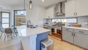 Een moderne keuken met een centraal eiland, roestvrijstalen apparatuur en een eethoek met een glazen tafel en stoelen.
