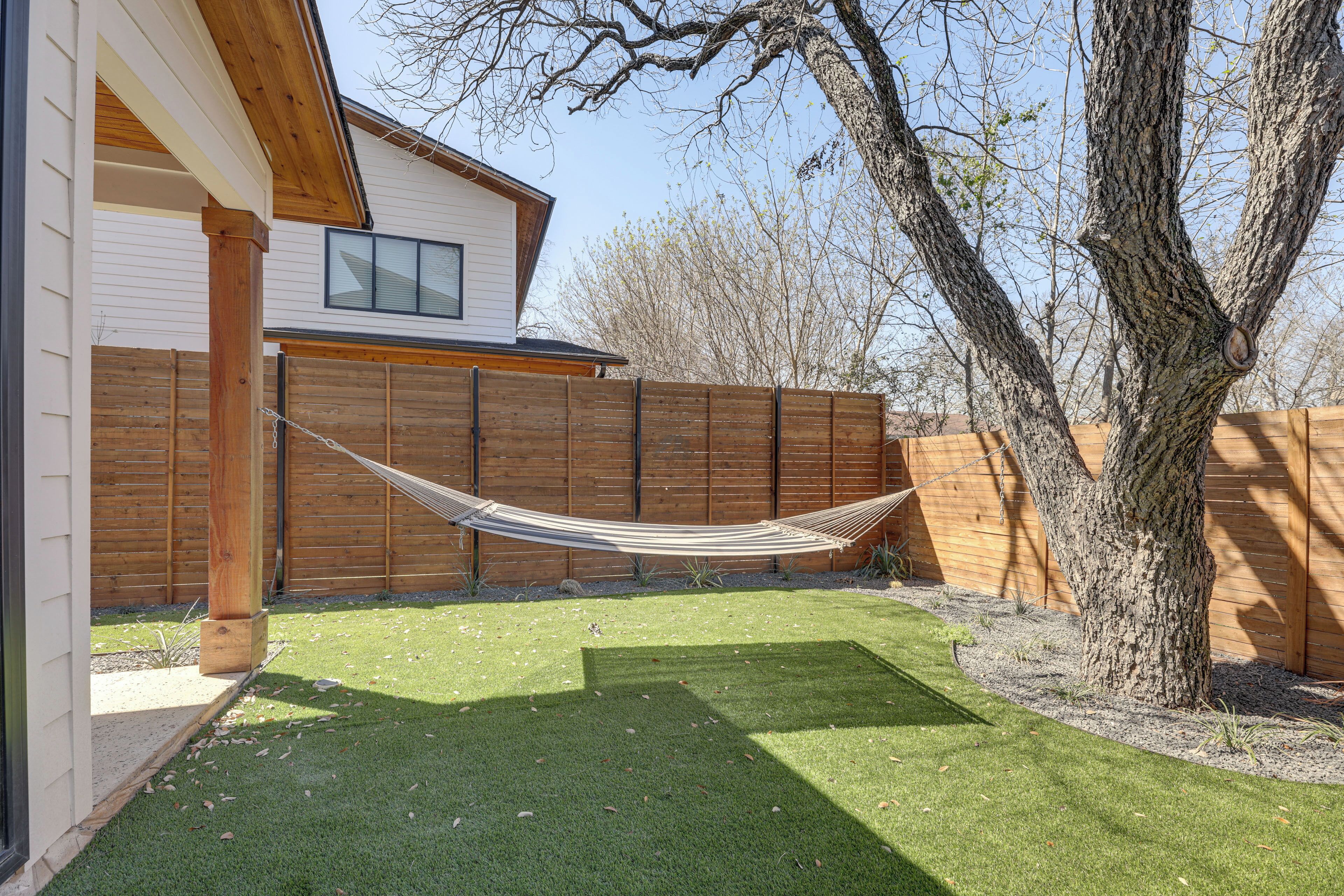 A backyard with a hammock, wooden fence, and a tree.