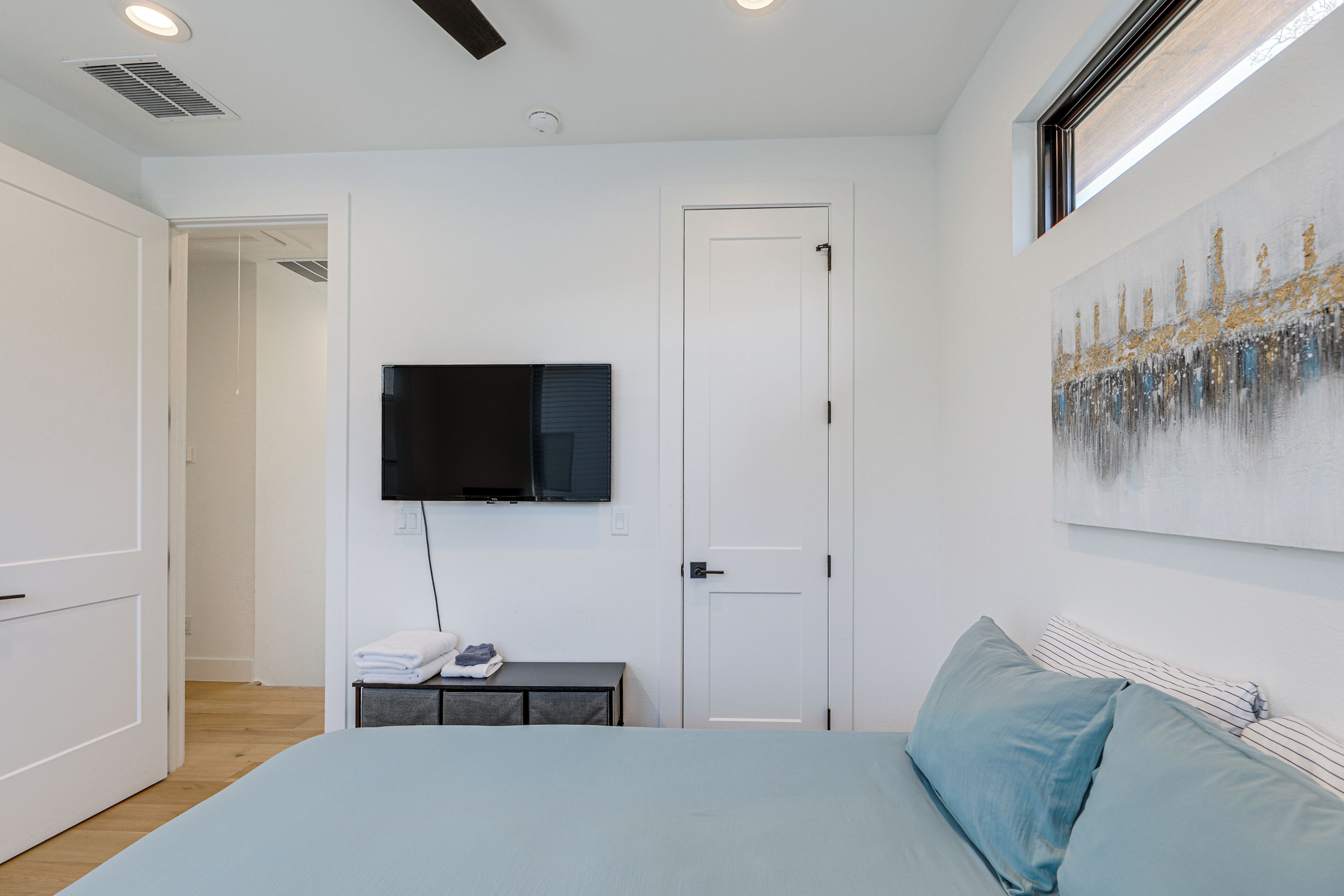 A bedroom with a bed, a TV mounted on the wall, a door, and a painting.