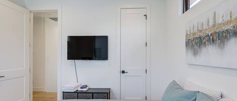A bedroom with a bed, a TV mounted on the wall, a door, and a painting.