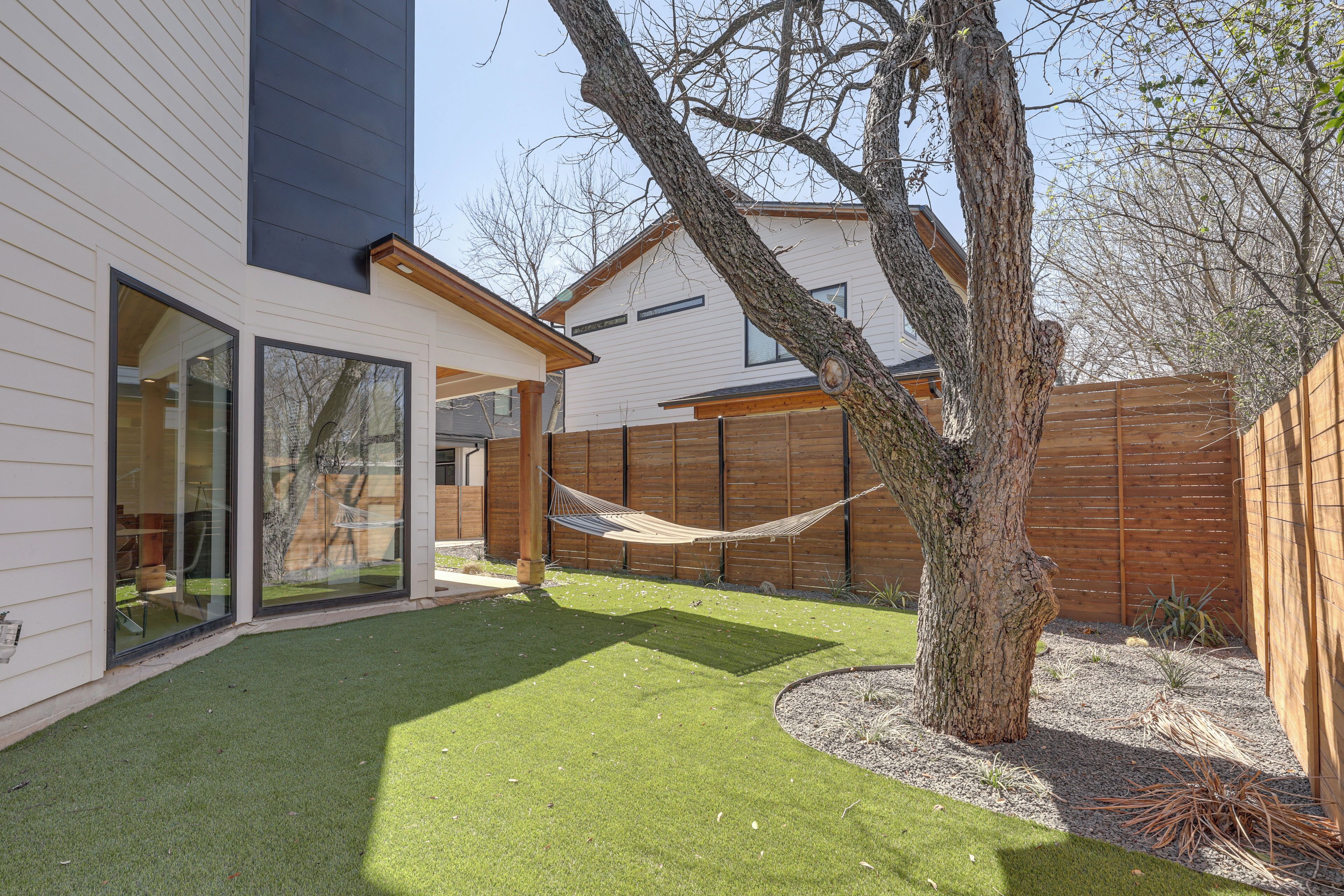 A modern house with a large glass door, a hammock, and a fenced yard.