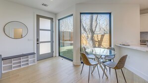 Een moderne keuken met een glazen eettafel en stoelen, een inbouwbank en een groot raam met uitzicht op een achtertuin.