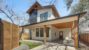 Een modern huis met twee verdiepingen, een overdekt terras, een houten schutting en een verzorgd gazon.