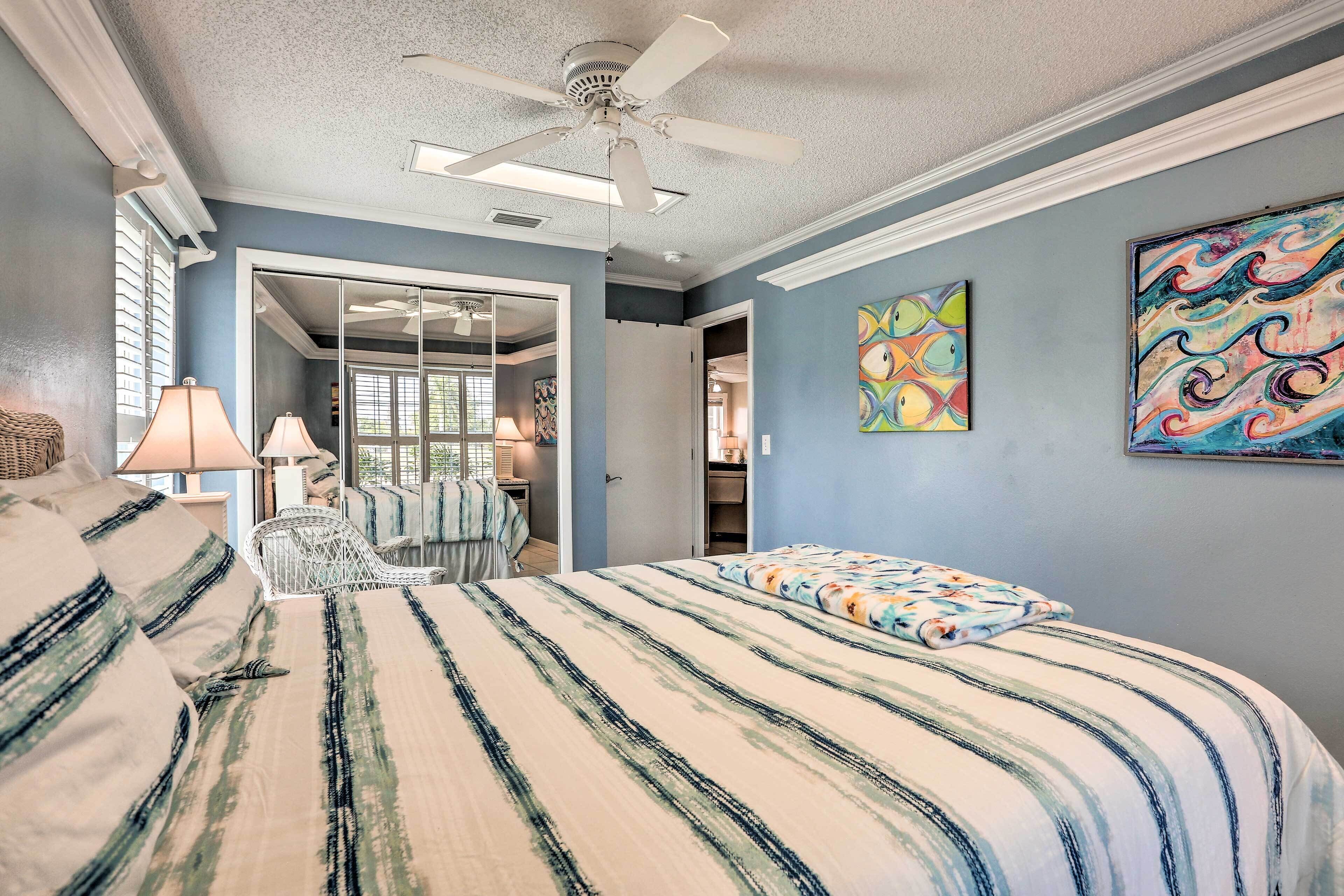 A bedroom with a bed, a ceiling fan, and two paintings on the wall.