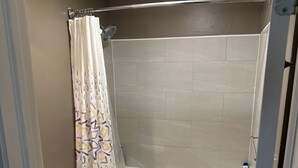 A bathroom with a toilet, a shower with a curtain, a bathtub, and a small rug on the floor.