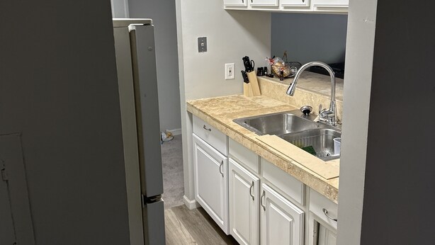 A kitchen with white cabinets, a stainless steel sink, and a light-colored countertop.