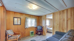 A room with wooden walls, a sofa, a chair, a television on a wooden stand, and a small table. - Rustic Cabin w/ Fire Pit, Steps to Sand Lake! (Stone Lake)