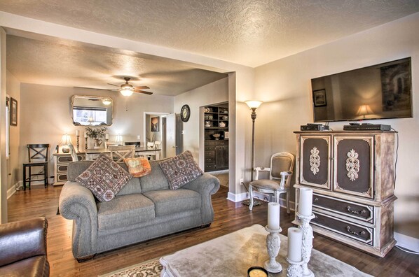 A living room with a grey sofa, a white cabinet, a television, and a ceiling fan. - Charming Downtown Coeur D'alene Home With Yard! (Coeur d'Alene)