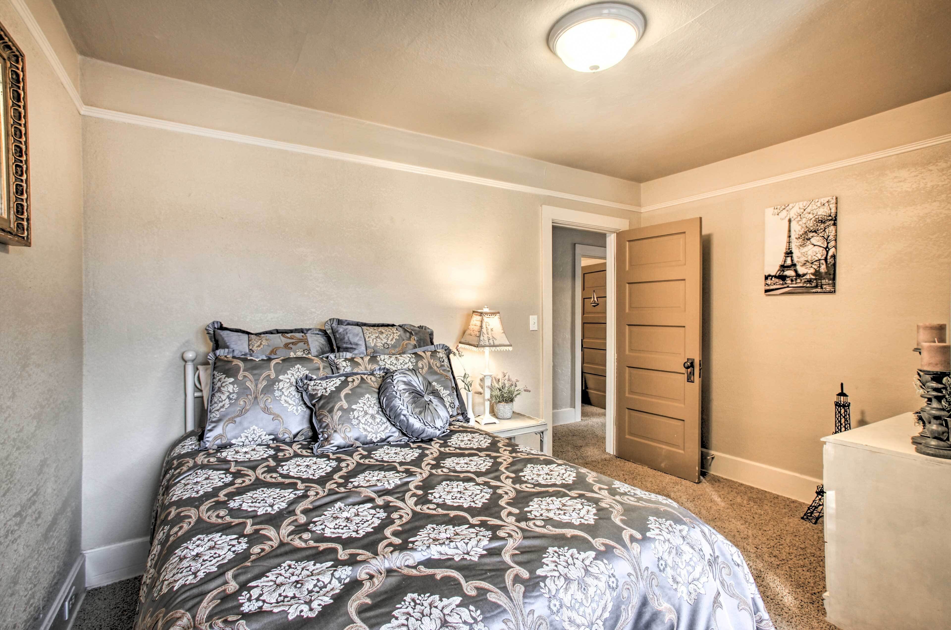 A bedroom with a bed, bedside table, lamp, and a door leading to another room.