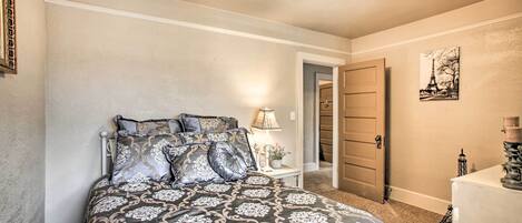 A bedroom with a bed, bedside table, lamp, and a door leading to another room.