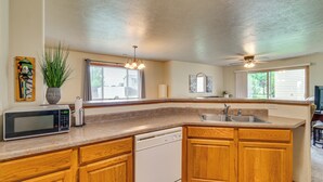 A kitchen with wooden cabinets, a built-in microwave, a dishwasher, and a large window providing natural light. - Cozy Sioux Falls House - Walk to Park! (Sioux Falls)