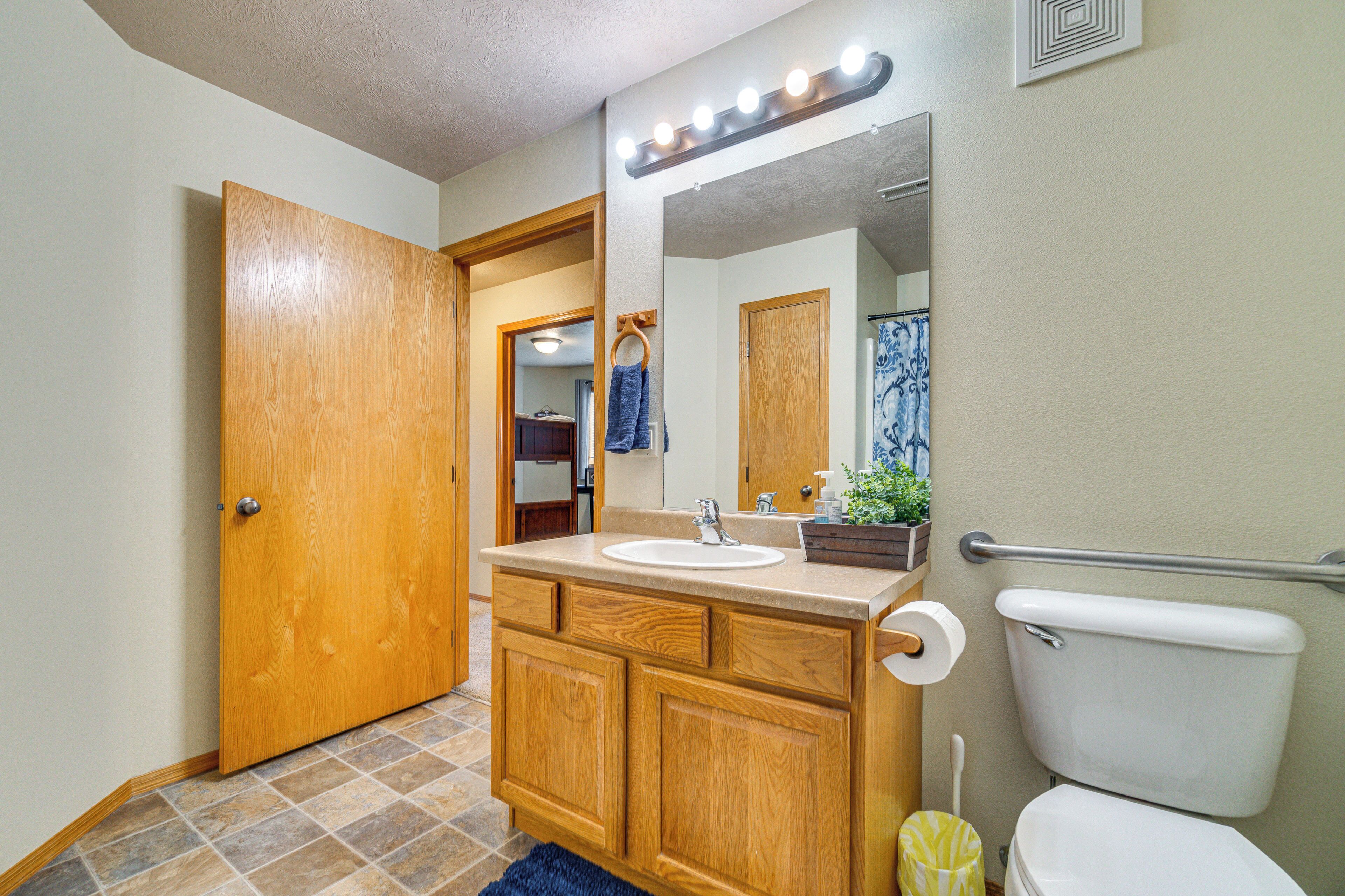Une salle de bain avec un meuble-lavabo en bois, un évier, un miroir avec éclairage intégré, des toilettes et un rideau de douche.