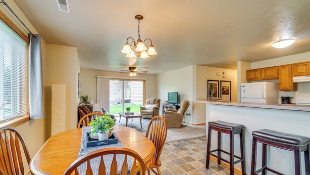 A spacious kitchen with wooden cabinets, a dining area with a wooden table and chairs, and a ceiling fan. - Cozy Sioux Falls House - Walk to Park! (Sioux Falls)