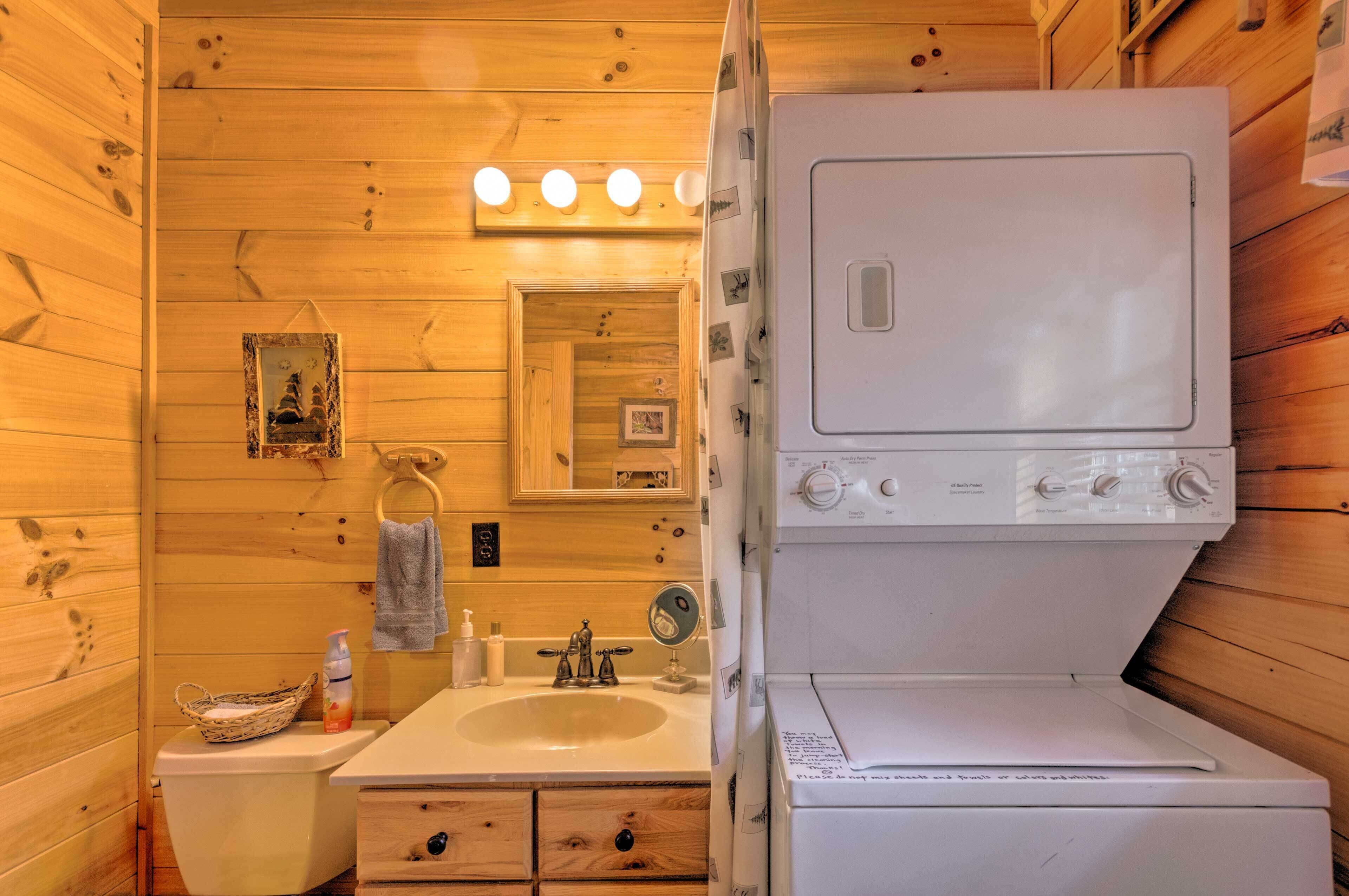 A compact wooden cabin bathroom with a sink, mirror, and stacked washer and dryer.