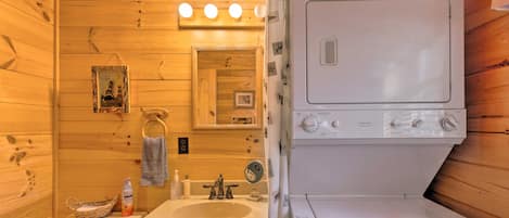 A compact wooden cabin bathroom with a sink, mirror, and stacked washer and dryer.