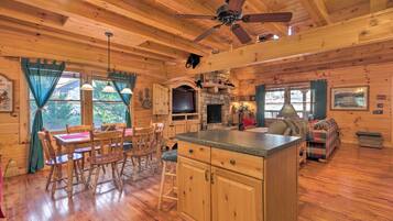 A cozy cabin interior with wooden floors, a dining area, a kitchen with granite countertops, and a ceiling fan.
