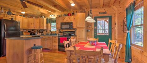 A wooden cabin kitchen with a central island, wooden chairs, a dining table, a ceiling fan, and a microwave.