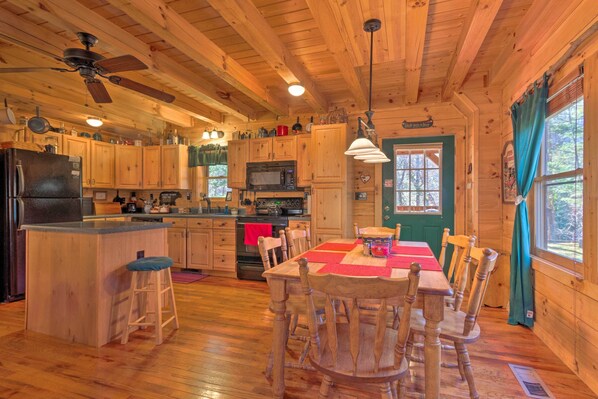 Cocina de cabaña de madera con una isla central, sillas de madera, una mesa de comedor, un ventilador de techo y un microondas.