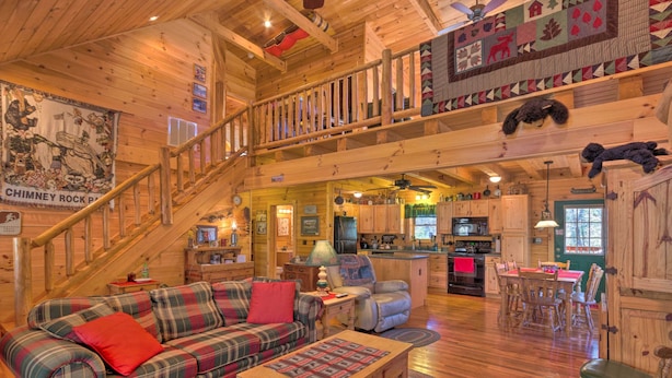 Ein gemütliches Blockhaus-Interieur mit einer Holztreppe, einem Karomuster-Sofa, einem Essbereich und einer Küche.