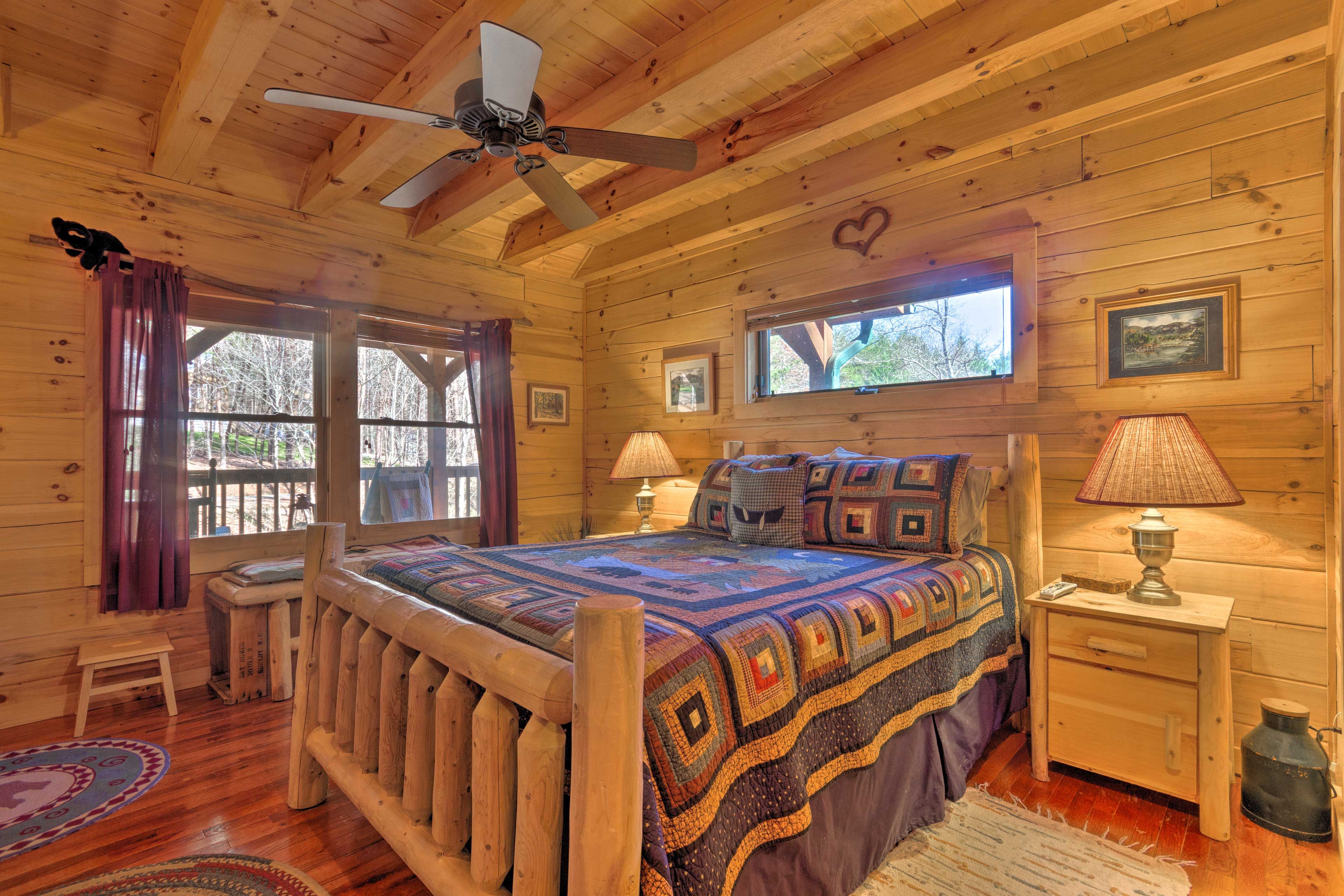 A cozy log cabin bedroom with a wooden bed, two bedside lamps, a small table, and a ceiling fan.
