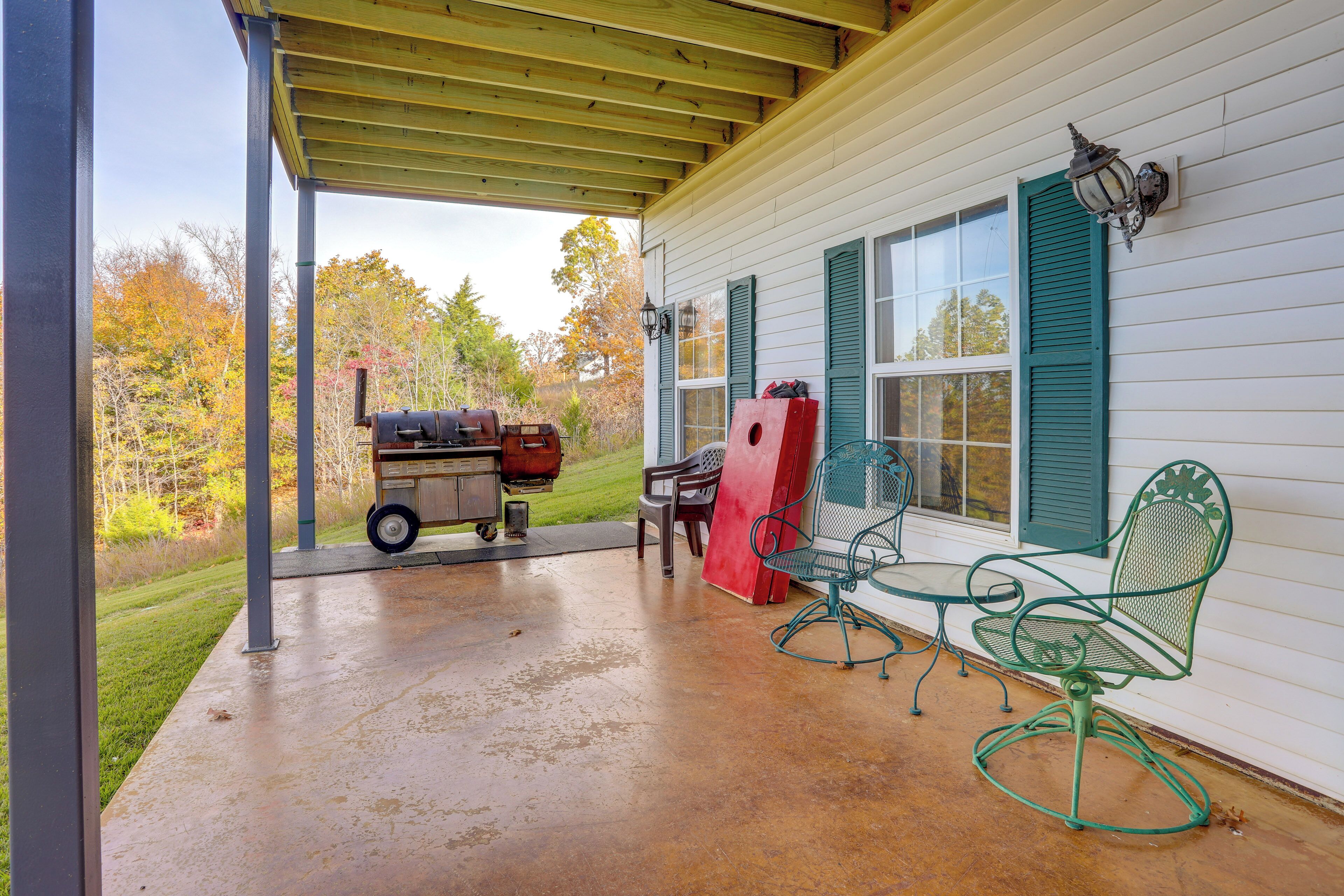 A covered patio with a grill, outdoor chairs, and a wooden deck.