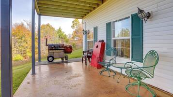 A covered patio with a grill, outdoor chairs, and a wooden deck.