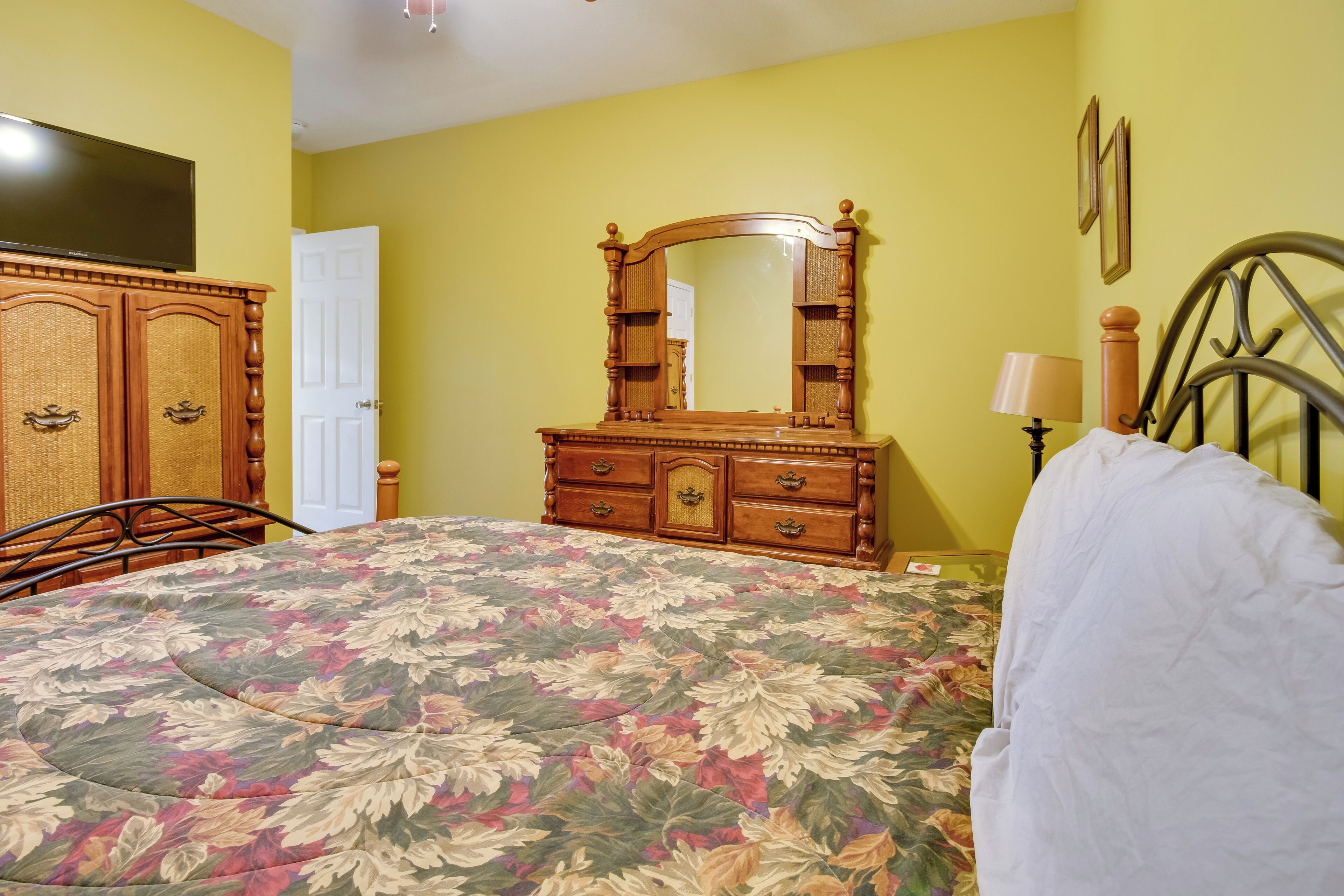 Un dormitorio con colcha estampada, cómoda de madera y espejo.