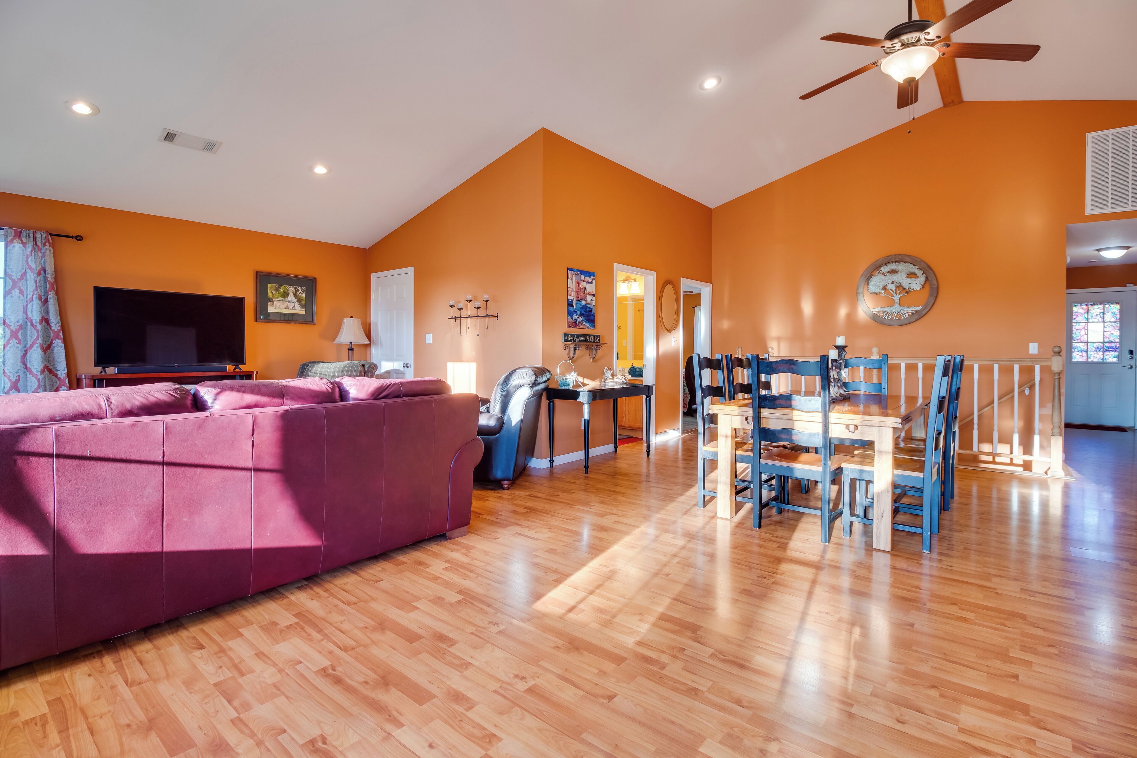 A spacious living room with a large sofa, a dining table with chairs, a ceiling fan, and a TV.